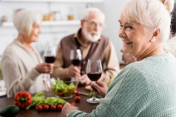 happy-senior-woman-holding-glass-red-wine-retired-friends-blurred